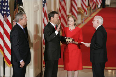 El Presidente George W. Bush observa el jueves, 29 de septiembre de 2005 en el East Room de la Casa Blanca en Washington mientras el Juez John G. Roberts toma el cargo de Presidente de la Corte Suprema ante el Juez de la Corte Suprema John Paul Stevens. La esposa del Juez Roberts, Jane, sostiene La Biblia.