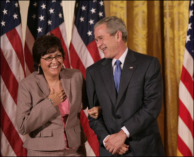 El Presidente George W. Bush está parado de lado de María Hines de Albuquerque, Nuevo México, quien fue galardonada con el Volunteer Service Award el viernes, 7 de octubre de 2005 en el East Room de la Casa Blanca, donde el Presidente Bush honró a seis personas con el premio presidencial al servicio voluntario como parte de la celebración del Mes de la Hispanidad.