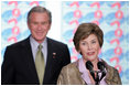 President George W. Bush stands by as he listens to remarks by Mrs. Bush on World AIDS Day before being introduced to the audience at the Dwight D. Eisenhower Executive Office Building Thursday, Dec. 1, 2005.