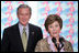 President George W. Bush stands by as he listens to remarks by Mrs. Bush on World AIDS Day before being introduced to the audience at the Dwight D. Eisenhower Executive Office Building Thursday, Dec. 1, 2005.