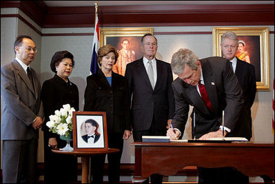 President George W. Bush signs a condolence book for the victims of the recent tsunami during a visit to the Embassy of Thailand in Washington, D.C., Monday, Jan. 3, 2005. Next to the book, stands a photograph of Khun Poom Jensen, 21. A grandson of Thailand's King Bhumibol Adulyadej, Mr. Jensen died in the tsunami. Also signing their condolences are Laura Bush and former Presidents Bush and Clinton.