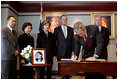 President George W. Bush signs a condolence book for the victims of the recent tsunami during a visit to the Embassy of Thailand in Washington, D.C., Monday, Jan. 3, 2005. Next to the book, stands a photograph of Khun Poom Jensen, 21. A grandson of Thailand's King Bhumibol Adulyadej, Mr. Jensen died in the tsunami. Also signing their condolences are Laura Bush and former Presidents Bush and Clinton.