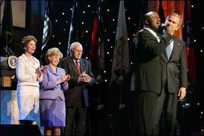 President George W. Bush puts his arm around Singer Bebe Winans as he sings 'God Bless America' during the 'Saluting Those Who Serve' event at the MCI Center in Washington, D.C., Tuesday, Jan. 18, 2005. Also pictured are, from left, Laura Bush, Lynne Cheney, and Vice President Dick Cheney.