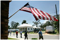 President George W. Bush waves as he is joined by Biloxi Mayor A.J. Holloway, left, Monday, Aug. 28, 2006, during President Bush's walking tour in the same Biloxi, Miss., neighborhood he visited following Hurricane Katrina in September 2005. The tour allowed President Bush the opportunity to assess the progress of the area's recovery and rebuilding efforts following the devastating hurricane.