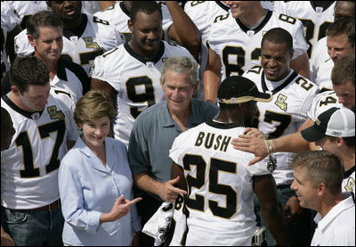 President George W. Bush and Laura Bush are surrounded by members of the New Orleans Saints football team Tuesday, Aug. 29, 2006, as they point out the name of Saints star rookie running back Reggie Bush, when the team met President Bush at the New Orleans Airport to pose for a team photo.