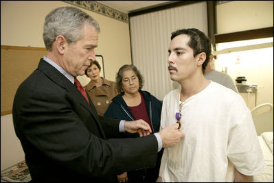 President George W. Bush presents the Purple Heart to U.S. Army Staff Sgt. Robert Cordero of El Paso, during a visit Friday, Dec. 22, 2006, to the Walter Reed Army Medical Center where the soldier is recovering from injuries suffered in Operation Iraqi Freedom. Looking on with Mrs. Laura Bush is Sgt. Cordero's mother, Rosa.