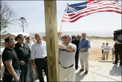 President George W. Bush watches as homeowner Jerry Akins places a flag outside his home Wednesday, March 8, 2006 in Gautier, Miss., on the site where the Akins family is rebuilding their home destroyed by Hurricane Katrina.