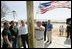 President George W. Bush watches as homeowner Jerry Akins places a flag outside his home Wednesday, March 8, 2006 in Gautier, Miss., on the site where the Akins family is rebuilding their home destroyed by Hurricane Katrina.