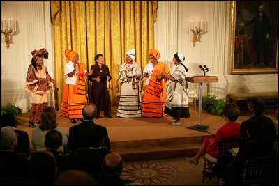 Mrs. Laura Bush listens to a performance from members of the Mothers to Mothers-To-Be representatives of South Africa, Monday, March 13, 2006 in the East Room of the White House. Mrs. Bush had earlier met with the members of the program, who mentor and counsel mothers who come for prenatal care to clinics and find they are HIV-positive, on her visit to South Africa in July of 2005. From left to right on stage are Aunt Manyongo "Kunene" Mosima Tantoh, Nosisi Mngceke, Patty Thomas, Gloria Ncanywa, Monica Abdullah and Babalwa Mbono.