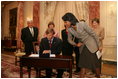 Mrs. Laura Bush, along with family of Ambassador Mark Dybul, watch as U.S. Secretary of State Condoleezza Rice assists newly sworn-in Ambassador Mark Dybul as he signs appointment documents Tuesday, October 10, 2006, during the swearing-in ceremony of Ambassador Mark Dybul in the Benjamin Franklin Room at the US Department of State in Washington, D.C.