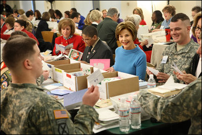 Mrs. Laura Bush is seated between volunteers Master Tre'shaad Cox, 11, left, and U.S. Army Sgt. Thomas Griffin, an out-patient at Walter Reed Army Medical Center, during a visit Saturday, Dec. 6, 2008, to the American Red Cross Holiday Mail for Heroes Packing Event at the Red Cross National Headquarters in Washington, D.C. Mrs. Bush reminded the volunteers that during this holiday season, "we are reminded of our many blessings, especially our freedom. The American Red Cross Holiday Mail for Heroes project, in partnership with Pitney Bowes, provides citizens an opportunity to send holiday cards to members of our Armed Forces. I am grateful to the many volunteers gathered here today to ensure our military receives our message of thanks for the sacrifice they make each day to defend our freedom."