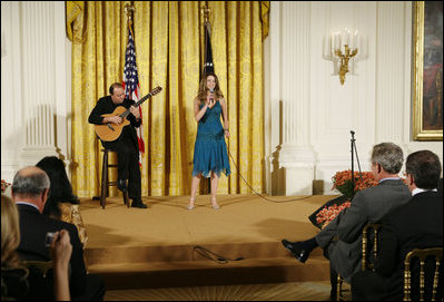 President George W. Bush, seated right-front, listens to the performance of singer Ana Cristina and guitarist Marco Linares, Friday, Oct. 6, 2006, in the East Room of the White House, in celebration of National Hispanic Heritage Month.