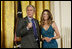 President George W. Bush joins singer Ana Cristina on stage to thank her and guitarist Marco Linares for their performance Friday, Oct. 6, 2006, in the East Room of the White House, in celebration of Hispanic Heritage Month.