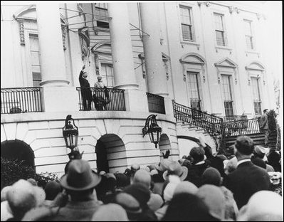 President Hoover waves to crowds at the 1929 Easter Egg Roll from the balcony of The White House. First Lady Lou Hoover, who introduced maypole and folk dancing activities to the event, smiles beside him. 