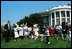 Former President Bush blows a whistle to start an egg roll race at the 1989 White House Easter Egg Roll while First Lady Barbara Bush smiles at the children participating.