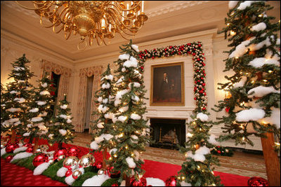 White tree lights twinkle in the shiny red and silver glass ornaments on the snow covered tabletop Christmas trees in the State Dinning Room.