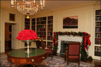 Silver containers filled with red carnations adorn the tables in the Library. The fireplace mantle is decorated with traditional green garland, accented with glass bulbs and red bows.