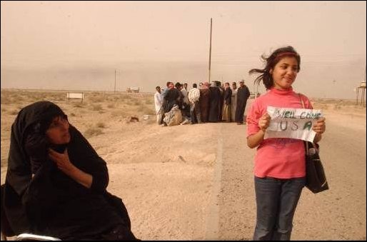 A local Iraqi girl shows her enthusiasm for the US being in Iraq with a homemade sign. Her family waits to find if one of their relatives is among the thousands of Enemy Prisoners of War (EPW) in a nearby EPW camp. (US Navy photo by PH1(SW) Aaron Ansarov) 