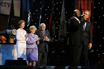 President George W. Bush puts his arm around Singer Bebe Winans as he sings 'God Bless America' during the 'Saluting Those Who Serve' event at the MCI Center in Washington, D.C., Tuesday, Jan. 18, 2005. Also pictured are, from left, Laura Bush, Lynne Cheney, and Vice President Dick Cheney.