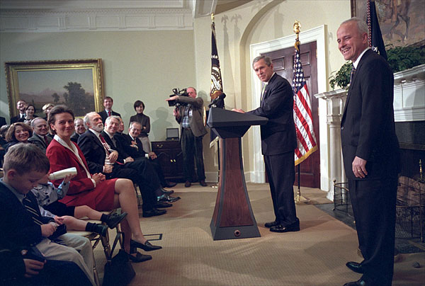 President George W. Bush and Jim Towey pause to smile at Mr. Towey's children during the Ceremony in which the President names him as the Director of the Faith-Based & Community Initiatives Director in the Roosevelt Room Feb. 1. "The purpose of this initiative recognizes the power of faith in helping heal some of our nation's wounds," said the President. "And today, I'm honored to name Jim Towey as its new head and new director. He has served a Republican senator and a Democratic governor. He understands there are things more important than political parties." White House photob by Eric Draper.