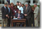 President George W. Bush signs the Job Creation and Worker Assistance Act of 2002 during a live radio address in the Rose Garden March 9, 2002. On hand for the signing were Senators Trent Lott (far left) and Tom Daschle (second from left) and Speaker of the House Dennis Hastert (standing to right of the President). "We're seeing some encouraging signs in the economy, but we can't stand by and simply hope for continued recovery," said President Bush. "We must work for it." White House photo by Eric Draper