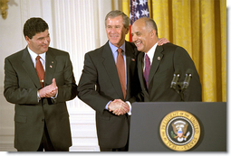 President George W. Bush embraces his nominee for Surgeon General, Dr. Richard Carmona, as Dr. Elias Zerhouni, left, applauds in the East Room Tuesday, March 26. Dr. Zerhouni is nominated to be the Director of the National Institute of Health. White House photo by Tina Hager.