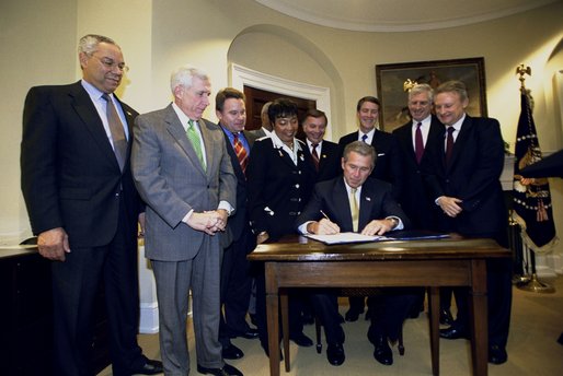 President George W. Bush signs the Sudan Peace Act in the Roosevelt Room at the White House, Oct. 21, 2002. Standing with the President are lawmakers and the Secretary of State Colin Powell, far left, and former Senator and special envoy for peace to the Sudan John Danforth, second from right. 