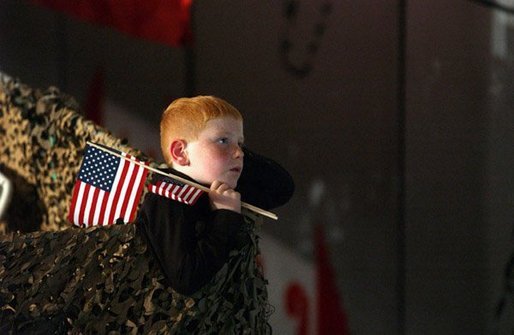 Keeping a grip on his souvenir flags, a boy listens to President George W. Bush at Pease Air National Guard Base in Portsmouth, N.H., Thursday, Oct. 9, 2003. White House photo by Tina Hager