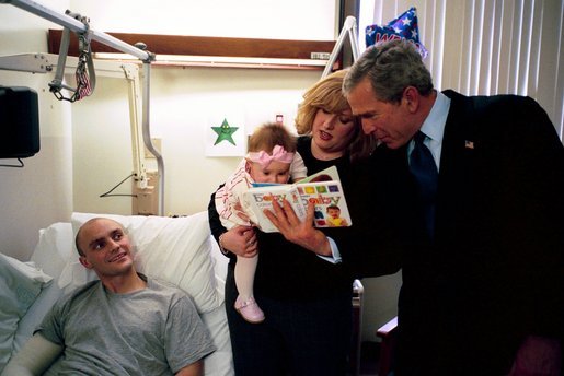 President George W. Bush reads a baby book with U.S. Army Reservist First Lieutenant Brandan Mueller of Webster Groves, Mo., his wife Amanda, and their daughter Abigail at Walter Reed Army Medical Center in Washington, D.C., Friday, March 19, 2004. Lt. Mueller was injured while serving in Operation Iraqi Freedom. White House photo by Eric Draper.