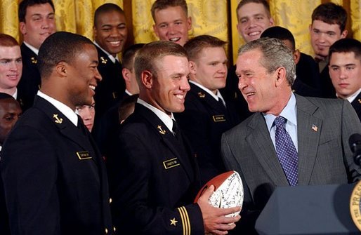 President George W. Bush laughs with Midshipmen Eddie Carthan, left, and team captain Craig Candeto during the presentation of the Commander-In-Chief Trophy to the U.S. Naval Academy football team in the East Room Monday, April 19, 2004. The trophy is awarded to the Service Academy with the year's best overall record in NCAA football games versus the other academies. White House photo by Tina Hager.