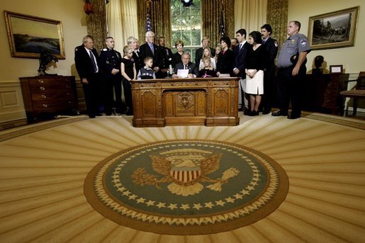 President George W. Bush delivers a Live Radio Address surrounded by Mrs. Bush and families of victims of 911 in the Oval Office, Saturday, Sept. 11, 2004. White House photo by Eric Draper