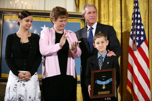 President George W. Bush places his hand on the shoulder of 11-year-old David Smith after he presented the young man with the Medal of Honor, awarded his father, Sgt. 1st Class Paul Smith, posthumously Monday during ceremonies at the White House. Joining David on stage are his step-sister Jessica and his mother, Birgit Smith.White House photo by Eric Draper