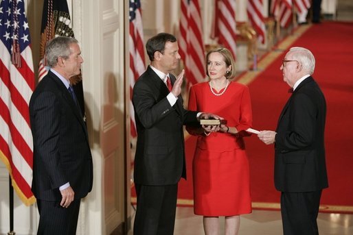 President George W. Bush watches Thursday, Sept. 29, 2005 in the East Room of the White House in Washington, as Judge John G. Roberts is sworn-in as the 17th Chief Justice of the United States by Associated Supreme Court Justice John Paul Stevens. Judge Roberts' wife Jane is seen holding the Bible. White House photo by Paul Morse