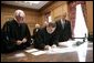 President George W. Bush looks on as U.S. Supreme Court Chief Justice John Roberts signs documents during his investiture ceremony at the U.S. Supreme Court, Monday, Oct. 3, 2005 in Washington. Associate Justice John Paul Stevens is seen at left, and Associate Justices Sandra Day O'Connor and Anthony Kennedy, background. White House photo by Eric Draper