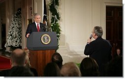 President George W. Bush listens as Terrence Hunt of The Associated Press delivers a question Monday, Dec. 19, 2005, during the President's press conference in the East Room of the White House. In response to Mr. Hunt's question, the President responded, "We're at war, and we must protect America's secrets."  White House photo by Paul Morse