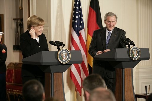 Chancellor Angela Merkel of Germany, adjusts her earpiece as President George W. Bush begins his remarks during a joint press availability Friday, Jan. 13, 2006, in the East Room of the White House. White House photo by Eric Draper