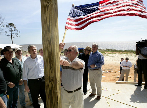 President George W. Bush watches as homeowner Jerry Akins places a flag outside his home Wednesday, March 8, 2006 in Gautier, Miss., on the site where the Akins family is rebuilding their home destroyed by Hurricane Katrina. White House photo by Eric Draper