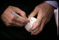 After warming up with a few pitches, President George W. Bush signs a baseball shortly before throwing one over the plate for the opening game between the Cincinnati Reds and the Chicago Cubs in Cincinnati, Ohio, Monday, April 3, 2006. White House photo by Eric Draper