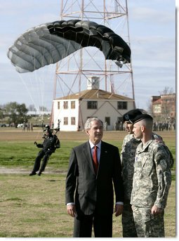 President George W. Bush speaks with U.S. Army Colonel Mike Linnington, center, and Sgt. 1st Class Mike Hertig, right, as he watches paratroopers from the U.S. Army Silver Wings Command exhibition team land Thursday, Jan. 11, 2006, during a demonstration of airborne infantry training at Fort Benning, Ga. White House photo by Eric Draper