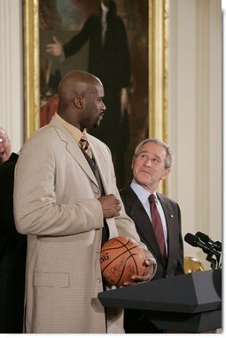 President George W. Bush looks up as he prepares to receive an autographed ball from Shaquille O'Neal Tuesday, Feb. 27, 2007, as the 2006 NBA champions visited the White House. The President told the East Room audience he was most impressed by the Heat's work in their Miami community and added, "I mean, I'm in awe of their athletic skills. Standing next to Shaq is an awe-inspiring experience."  White House photo by Paul Morse