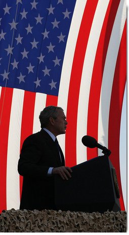 President George W. Bush stands in front of a U.S. flag Saturday, Jan. 12, 2008, as he addresses military personnel and coalition forces at Camp Arifjan in Kuwait. The President told the troops, "It's hard work you're doing, but it's necessary work." White House photo by Eric Draper