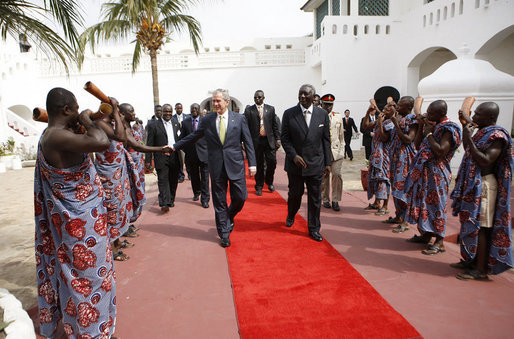 President George W. Bush, walking with Ghana President John Agyekum Kufuor, reaches out to shake hands with a ceremonial greeter on his arrival to Osu Castle, Wednesday, Feb. 20, 2008 in Accra, Ghana. White House photo by Eric Draper