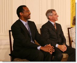 Dr. Benjamin Carson, left, seated with Dr. Anthony S. Fauci, listens Thursday, June 19, 2008, as he is announced as a recipient of the 2008 Presidential Medal of Freedom, at ceremonies in the East Room of the White House. White House photo by Shealah Craighead