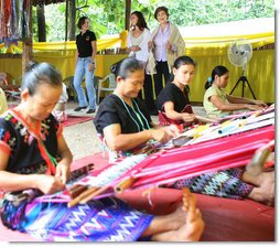 Mrs. Laura Bush and daughter Ms. Barbara Bush try on shawls created by weavers carrying on the traditional Karen ethnic craft at the Mae La Refugee Camp at Mae Sot, Thailand. In her August 7, 2008 comments, Mrs. Bush pointed out that the weavings are done to help generate money for the refugees and can be purchased via the Internet through consortiums that work with women at the camp. The camp houses at least 39,000 refugees waiting for a safe time to return to their home country. Many have decided the wait of 20 years has been too long and have immigrated to the United States and other countries. White House photo by Shealah Craighead