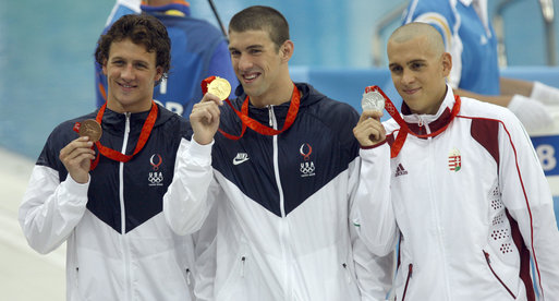 U.S. swimmer Michael Phelps shows off his Olympic gold medal as he stands on the victory podium with teammate Ryan Lochte, bronze medalist, and Hungary's Laszlo Cseh, silver medalist, at the National Aquatics Center in Beijing. White House photo by Eric Draper