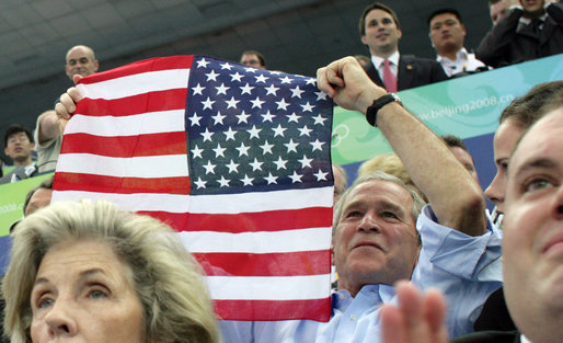 President George W. Bush displays an American flag as he cheers on the U.S. Olympic Swimming Team Sunday, Aug. 10, 2008, at the National Aquatics Center in Beijing. White House photo by Shealah Craighead