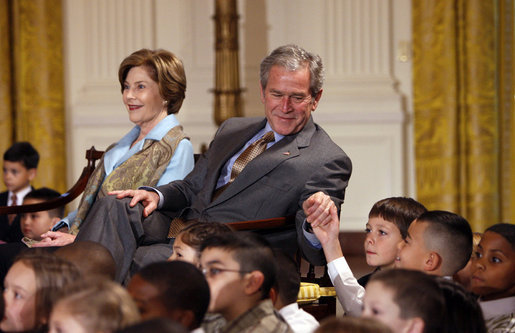 President George W. Bush, sitting with Mrs. Laura Bush, reaches to hold the hand of a young child Monday, Dec. 8, 2008 in the East Room of the White House, during the Children's Hoilday Reception and Performance. White House photo by Eric Draper