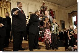 President George W. Bush is joined by two children on stage in the East Room of the White House as he thanks members of the musical group Sweet Heaven Kings, Monday, Dec. 8, 2008, during the Children's Holiday Reception and Performance. White House photo by Eric Draper