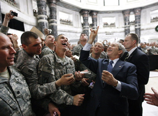 President George W. Bush gestures the "hook'em horns" sign of the University of Texas to U.S. military personnel in the balcony, as he meets with U.S. military and diplomatic personnel Sunday, Dec, 14, 2008, at the Al Faw Palace-Camp Victory in Baghdad. White House photo by Eric Draper