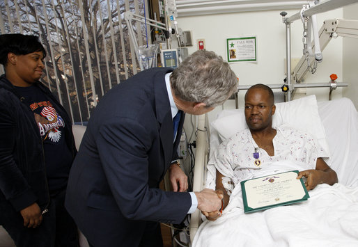 President George W. Bush shakes the hand of U.S. Army Sgt. First Class Neal Boyd of Haynesville, La., after presenting him a Purple Heart during a visit Monday, Dec. 22, 2008, to Walter Reed Army Medical Center, where the soldier is recovering from injuries received in Operation Iraqi Freedom. Looking on is SFC Boyd's wife, Joyce. White House photo by Eric Draper